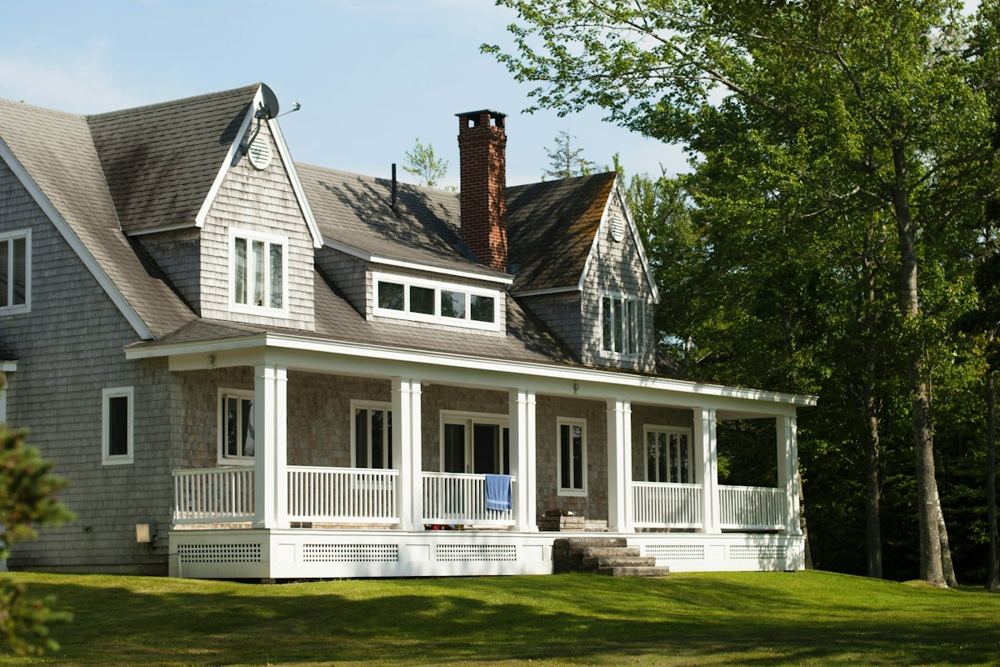A shingled Massachusetts house with a wide front porch and gutters along the roof line