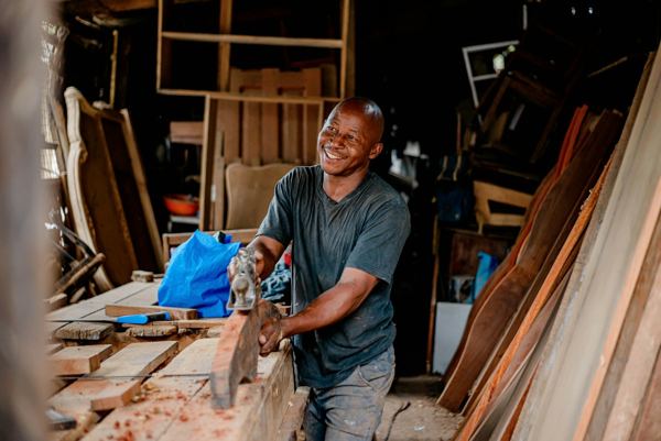 A carpenter smiling while working on a piece of wood
